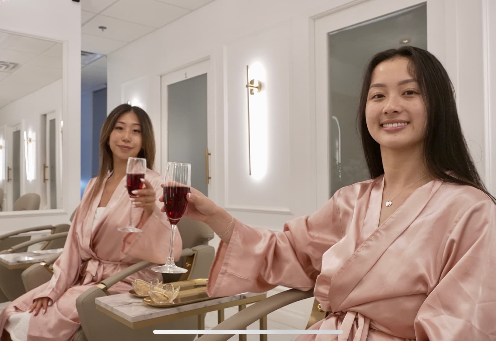 Two friends toasting wine in pink robes